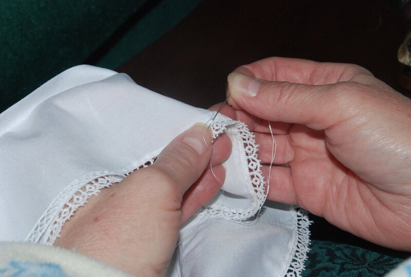 Kingdom Gowns artisan hand-applying lace trim to an ivory christening gown using needle and thread — Michigan