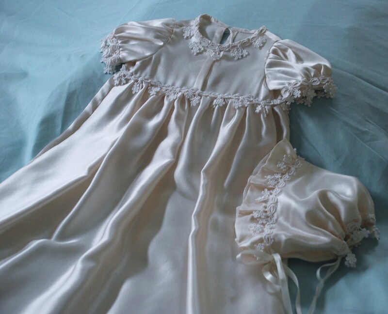 Ivory satin christening gown displayed with matching daisy-pattern lace bonnet — Kingdom Gowns Michigan